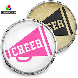 Può includere: Due bottoni rotondi con bordo argentato. Uno presenta un megafono rosa con la scritta "CHEER" in bianco. L'altro ha un megafono nero con "CHEER" in lettere dorate su sfondo strutturato. Testo in alto: "SNAP ACCENTS" e "CUSTOMIZE COLOR".