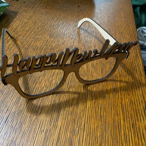 Könnte beinhalten: Holzbrille mit der Aufschrift "Happy New Year". Die Brille ist braun und hat ein weißes Band oben.