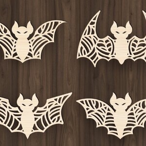 May include: Four laser cut wooden bat silhouettes with intricate designs. The bats are white and have a web-like pattern.