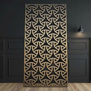 May include: A gold metal room divider with a geometric pattern of circles and triangles. The divider is standing in front of a black wall with white trim.