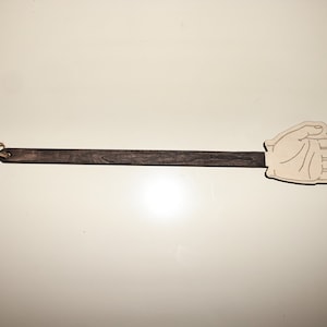 Puede incluir: Un matamoscas de madera con un diseño en forma de mano. El matamoscas tiene un mango de madera marrón oscuro y una paleta en forma de mano marrón claro.