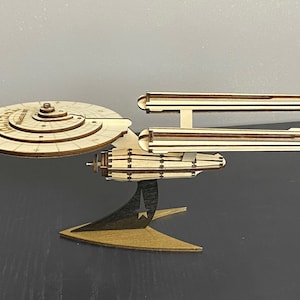 Puede incluir: Un modelo de madera de la nave espacial USS Enterprise de Star Trek. El modelo está ensamblado y presenta un diseño detallado con una sección de platillo, nacelas y una base.