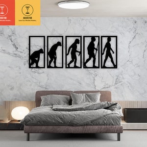 Puede incluir: Arte de pared de metal negro que representa las etapas de la evolución humana. El arte presenta cinco figuras en línea, comenzando con una figura simiesca agachada y terminando con una figura humana moderna caminando erguida. El arte está montado en una pared blanca sobre un sofá gris.