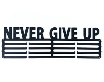 以下が含まれることがあります： 「NEVER GIVE UP」という文字が太字で書かれた黒い金属製のメダルディスプレイラック。ラックにはメダルを収納できるスロットが10個あります。