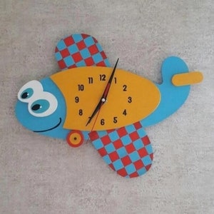 May include: A blue and yellow airplane-shaped clock with red and blue checkered wings. The clock face has black hands and white numbers.