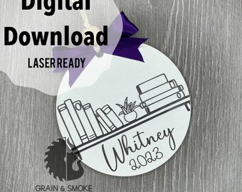 May include: A white round ornament with a black and white illustration of a bookshelf with books and a plant. The text "Whitney 2023" is written below the bookshelf.