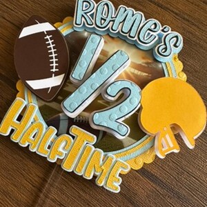 May include: A blue and yellow cake topper with the text "Rome's 1/2 Halftime" and a football, helmet, and number 2.
