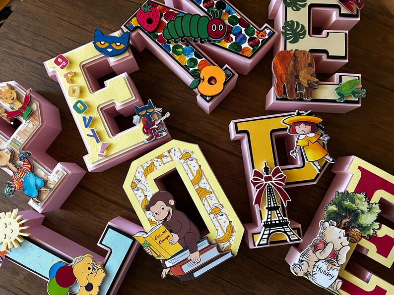 May include: A collection of three-dimensional block letters in various colors, decorated with cutouts of children's book characters including a caterpillar, a monkey reading a book, a bear, and an Eiffel Tower, with the word GROOVY printed on one letter.