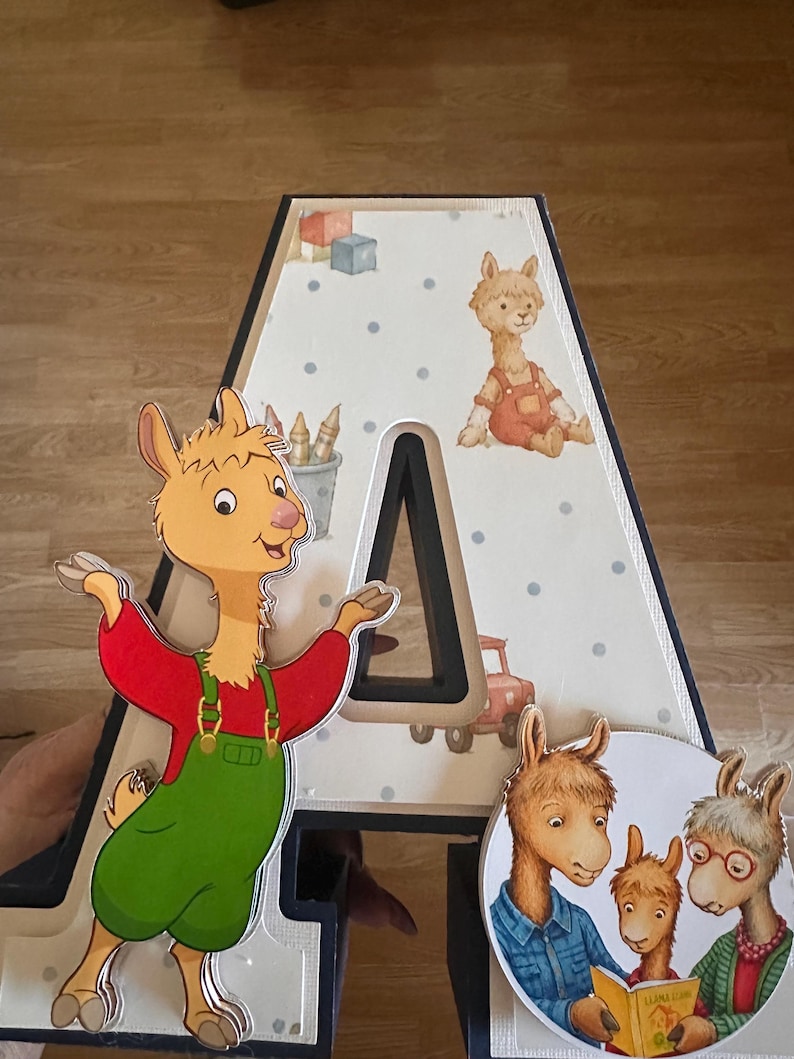 May include: A large, three-dimensional letter A featuring a light-colored background with blue polka dots and illustrations of toys. A cartoon llama in green overalls is attached to the left, and a circular image of three llamas is on the right.