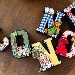 May include: A set of six three-dimensional letters spelling CONNOR, each decorated with various children's book characters and themes, including Curious George, Monsters Inc, Winnie the Pooh, The Cat in the Hat, and Clifford the Big Red Dog.