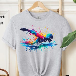 May include: A grey t-shirt with a colorful graphic of a swimmer in a splash of paint. The text "Sport Grey" is visible in the top left corner of the image.