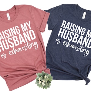 May include: Two t-shirts with the text "Raising my Husband is exhausting" in white on a pink and a blue shirt.