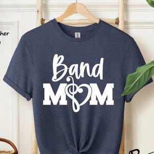 May include: A heather navy blue t-shirt with the text "Band Mom" in white, featuring a musical note and a heart.