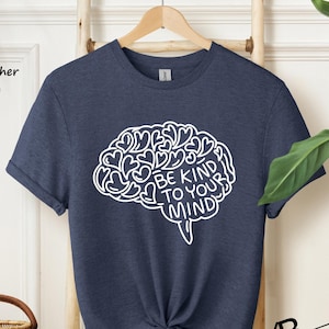 May include: A navy blue heather t-shirt with a white outline of a brain with hearts and the text "Be Kind To Your Mind".