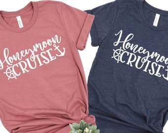 May include: Two t-shirts with the text "Honeymoon Cruise" in white lettering. One shirt is a dusty rose color and the other is a dark blue.