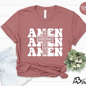 May include: A heather mauve t-shirt with a white graphic of a cross and the word "Amen" repeated three times in a retro font.