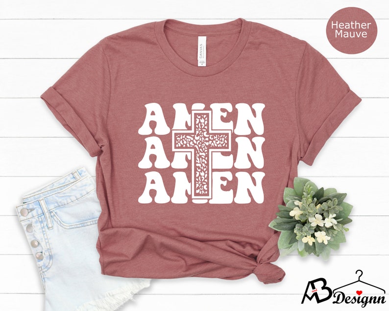 May include: A heather mauve t-shirt with a white graphic of a cross and the word "Amen" repeated three times in a retro font.