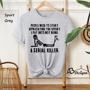 May include: A gray t-shirt with a black skeleton graphic and the text "PEOPLE NEED TO START APPRECIATING THE EFFORT I PUT INTO NOT BEING A SERIAL KILLER".