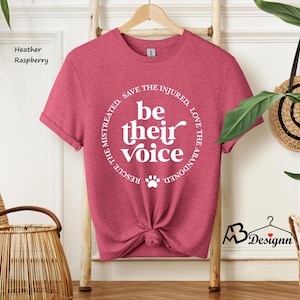 May include: Heather raspberry t-shirt with the text "be their voice" in a circular design. The design includes a paw print and the phrases "Rescue the mistreated, save the injured, love the abandoned."