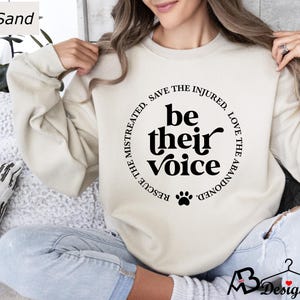 May include: A beige sweatshirt with a black paw print and the text "Rescue the mistreated, save the injured, love the abandoned. Be their voice." printed on the front.