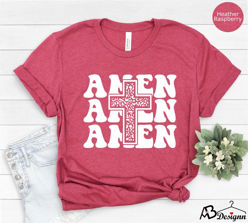 May include: A heather raspberry t-shirt with a white graphic of the word "Amen" repeated three times with a cross in the center. The cross is filled with a white floral pattern.