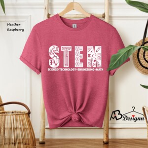 May include: Heather raspberry t-shirt with a white graphic that says "STEM" with icons representing science, technology, engineering, and math. The text below the graphic says "SCIENCE TECHNOLOGY ENGINEERING MATH".