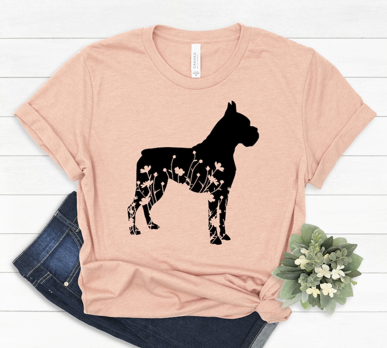 K&ouml;nnte beinhalten: Ein hellrosa T-Shirt mit einer schwarzen Silhouette eines Boxerhundes mit floralen Details innerhalb der Silhouette.