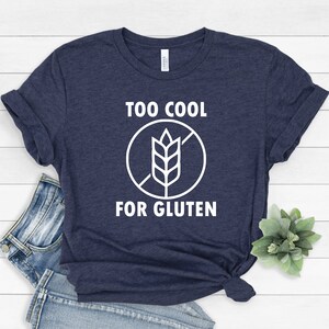 May include: A navy blue t-shirt with white text that reads "Too Cool For Gluten" and a white graphic of a wheat stalk with a diagonal line through it.