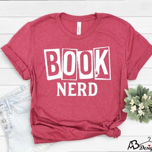 Może przedstawiać: Czerwony T-shirt z nadrukiem "BOOK NERD" w kolorze białym z przodu.
