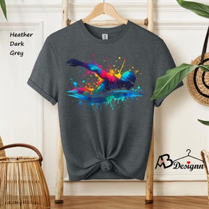 May include: A dark heather grey t-shirt with a colorful watercolor design of a swimmer. The design features splashes of blue, green, yellow, orange, and red.