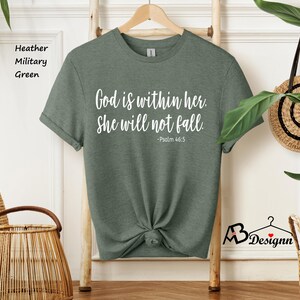 Peut inclure: Un t-shirt vert militaire chin&eacute; avec le texte "Dieu est en elle. Elle ne tombera pas. -Psaume 46:5" imprim&eacute; en blanc.