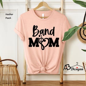 May include: A peach-colored t-shirt with the text "Band Mom" in black lettering. A musical note and heart are included in the design.