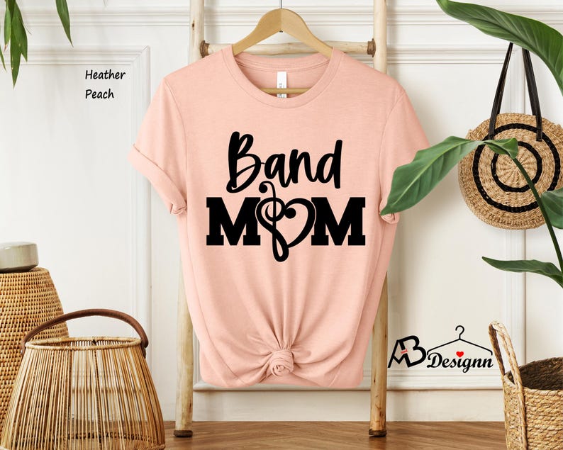 May include: A peach-colored t-shirt with the text "Band Mom" in black lettering. A musical note and heart are included in the design.