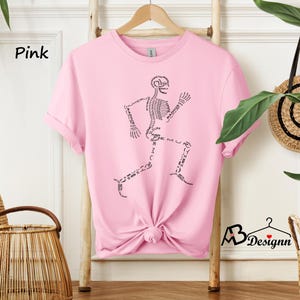May include: Pink t-shirt with a black skeleton graphic. The skeleton is running and has the names of the bones written on it.