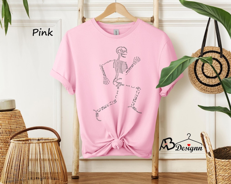 May include: Pink t-shirt with a black skeleton graphic. The skeleton is running and has the names of the bones written on it.