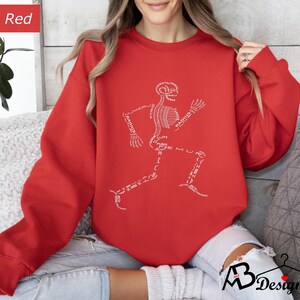 Peut inclure: Un sweat-shirt rouge avec un motif de coureur squelettique blanc. Les os du squelette sont &eacute;tiquet&eacute;s avec des termes anatomiques. Le sweat-shirt a des manches longues et un col rond. Le mot "Red" est dans un encadr&eacute; rouge en haut &agrave; gauche.