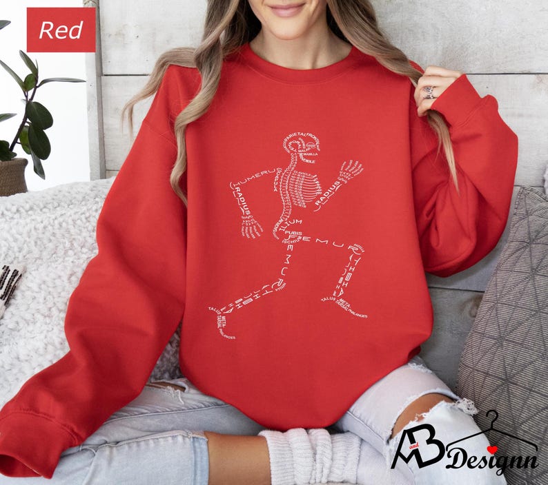 Peut inclure: Un sweat-shirt rouge avec un motif de coureur squelettique blanc. Les os du squelette sont &eacute;tiquet&eacute;s avec des termes anatomiques. Le sweat-shirt a des manches longues et un col rond. Le mot "Red" est dans un encadr&eacute; rouge en haut &agrave; gauche.