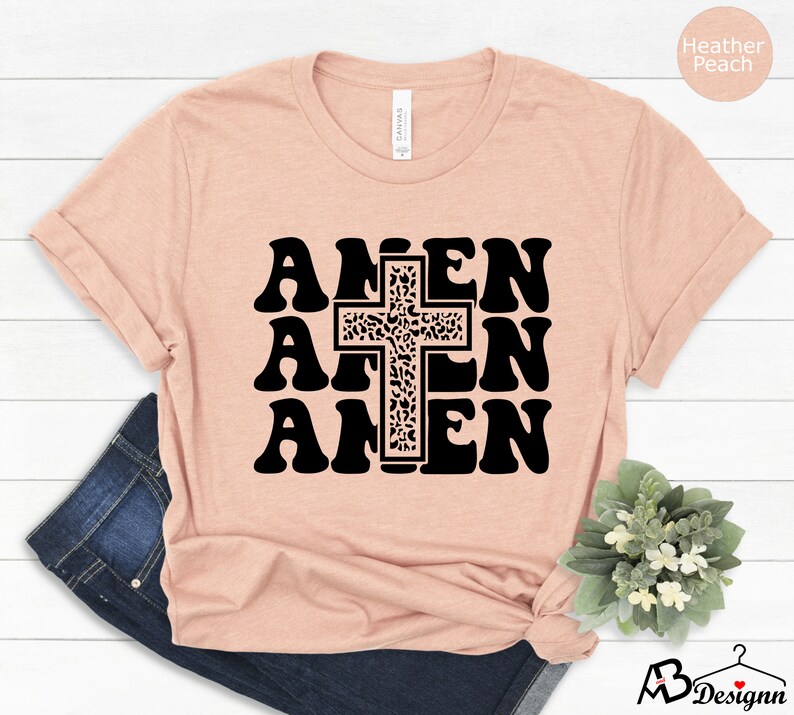 May include: A heather peach t-shirt with a black graphic of the word "Amen" repeated three times with a cross in the center. The cross is decorated with a leopard print pattern.