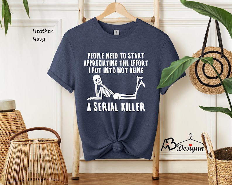 May include: A navy blue t-shirt with a white skeleton graphic and the text "PEOPLE NEED TO START APPRECIATING THE EFFORT I PUT INTO NOT BEING A SERIAL KILLER".