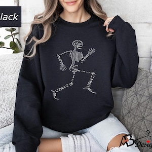 Peut inclure: Sweat-shirt noir avec un motif de coureur squelettique blanc et des &eacute;tiquettes d'os. Le mot "Black" est dans un encadr&eacute; blanc en haut &agrave; gauche. Un style de sweat-shirt confortable et d&eacute;contract&eacute;.