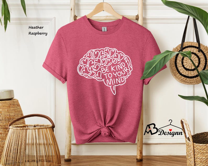 May include: Heather raspberry colored t-shirt with a white outline of a brain with hearts inside and the text "Be Kind To Your Mind".