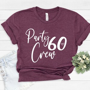 May include: A maroon t-shirt with the text "Party 60 Crew" in white lettering. The number 60 has a small white heart next to it.