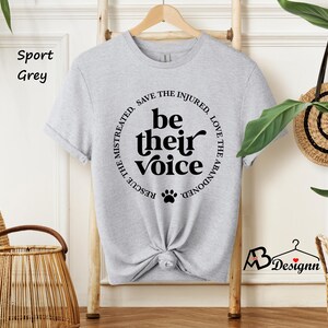 May include: Sport grey t-shirt with the text "be their voice" in a circular design. The design includes a paw print and phrases like "rescue the mistreated" and "love the abandoned".