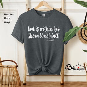 Peut inclure: Un t-shirt gris chin&eacute; fonc&eacute; avec le texte "God is within her. She will not fall. -Psalm 46:5" imprim&eacute; en blanc.