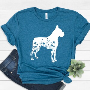 K&ouml;nnte beinhalten: Ein blaues T-Shirt mit einer wei&szlig;en Silhouette eines Boxerhundes mit Blumen in der Silhouette.