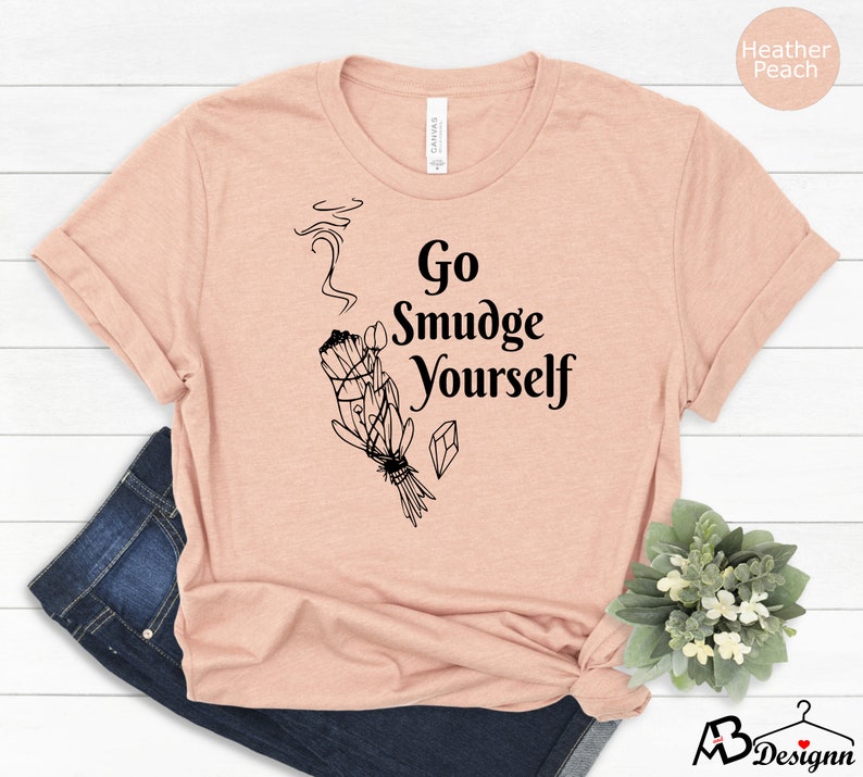 K&ouml;nnte beinhalten: Ein T-Shirt in der Farbe Heidelbeer-Pfirsich mit einem schwarzen Aufdruck eines R&auml;ucherstabs und dem Text "Go Smudge Yourself".