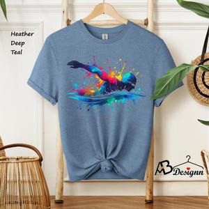May include: A heather deep teal t-shirt with a colorful graphic of a swimmer in a splash of water. The graphic is made up of various colors, including red, orange, yellow, green, blue, and purple.