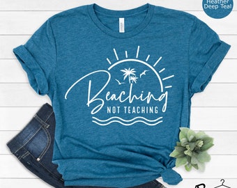 May include: A teal blue t-shirt with white text that reads "Beaching Not Teaching" with a sun, palm trees, and waves graphic.