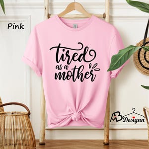 May include: Pink t-shirt with the text "tired as a mother" in black lettering.