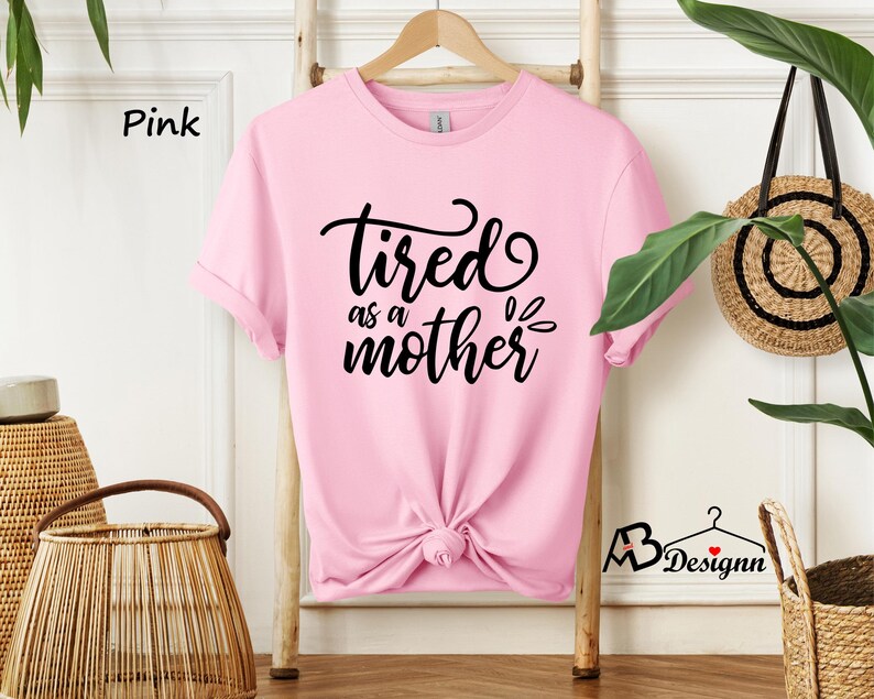 May include: Pink t-shirt with the text "tired as a mother" in black lettering.
